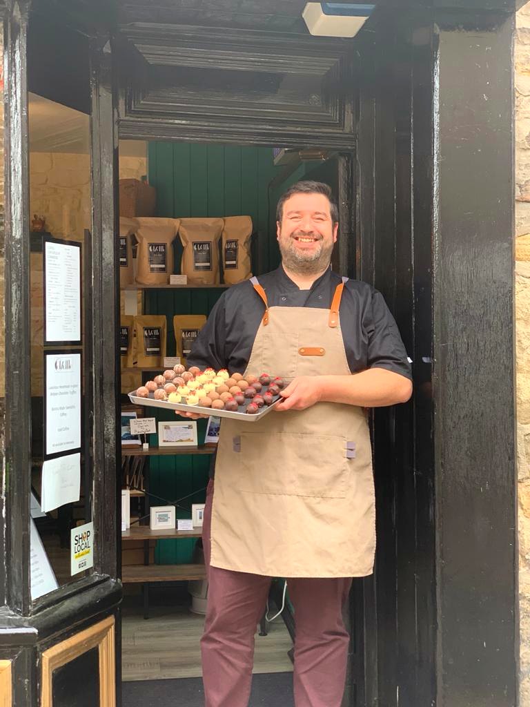 Phil Weddle, Coffuffle's owner, in an apron in the shop doorway, holding a tray of truffles